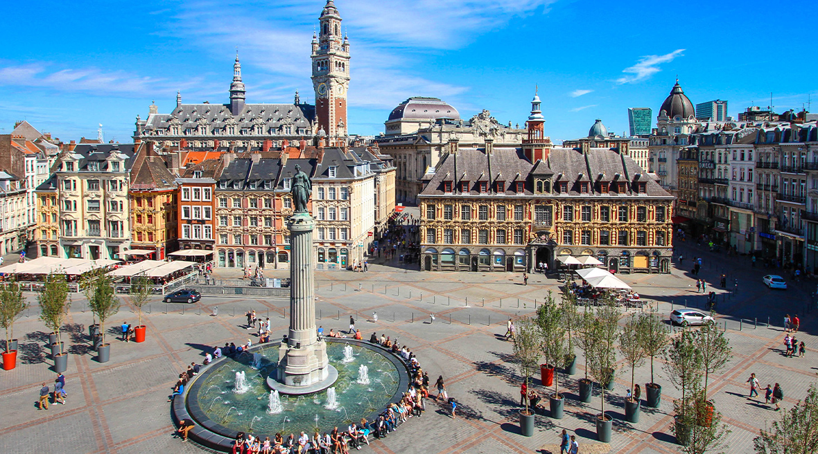 A large European city square with a monumental pillar and fountain and people walking and milling about